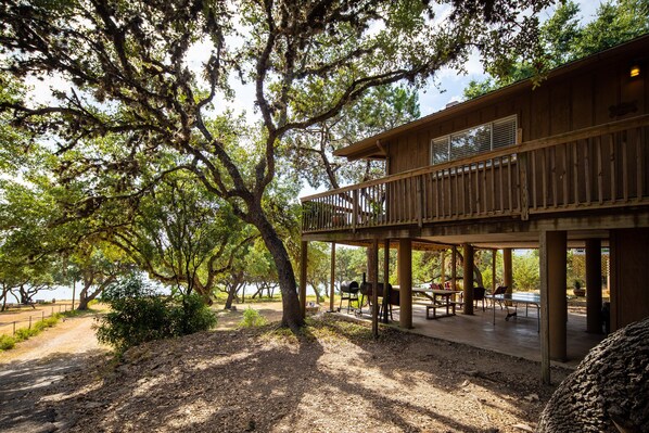A wooden cabin with a deck, surrounded by trees and a gravel path.