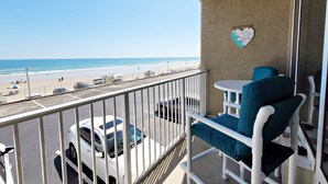 Un balcón con vistas a la playa, un coche blanco estacionado al fondo y una decoración con forma de corazón en la pared.