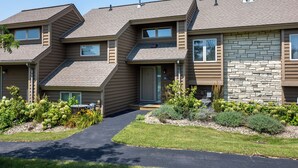 A modern multi-story residential building with a stone facade, a covered entryway, and a landscaped front yard. - Amazing Golf Views, Fireplace & Pool Access! (Galena)