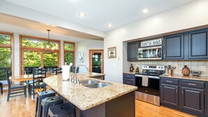 A modern kitchen with granite countertops, stainless steel appliances, and dark cabinetry. There is a dining area with wooden chairs and a large window offering a view of greenery. - Longwood - Wood Burning Fireplace - Hot Tub - Pool Table - Arcade Game (Galena)