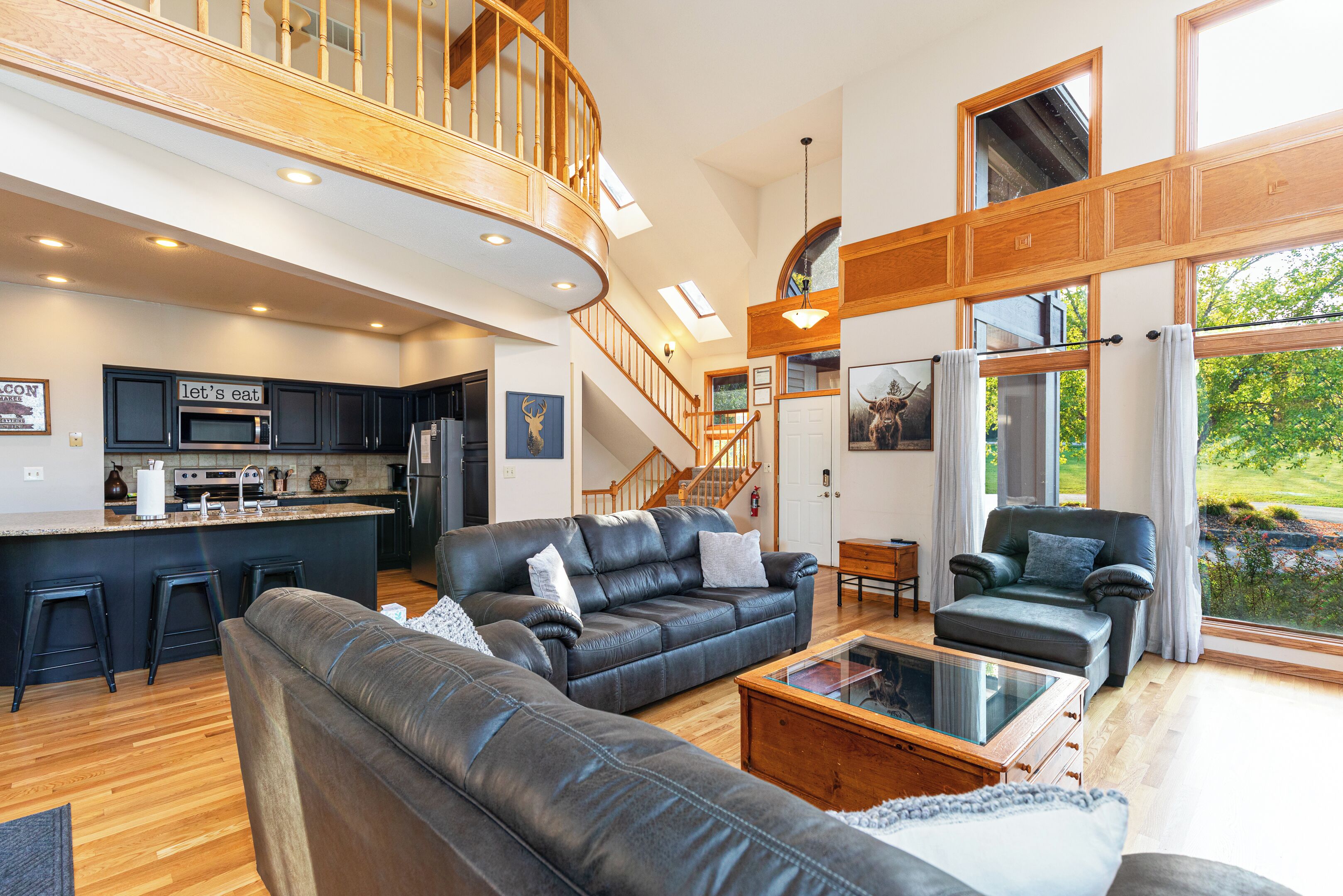 A spacious living area with a large leather sofa, a coffee table, and a view of the kitchen and outdoor space.