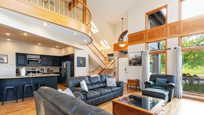 A spacious living area with a large leather sofa, a coffee table, and a view of the kitchen and outdoor space. - Longwood - Wood Burning Fireplace - Hot Tub - Pool Table - Arcade Game (Galena)