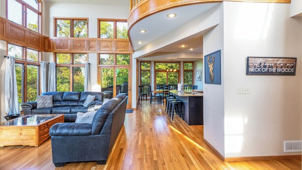 A spacious living area with a large sectional sofa, wooden flooring, and a view of the outdoors through large windows. - Longwood - Wood Burning Fireplace - Hot Tub - Pool Table - Arcade Game (Galena)