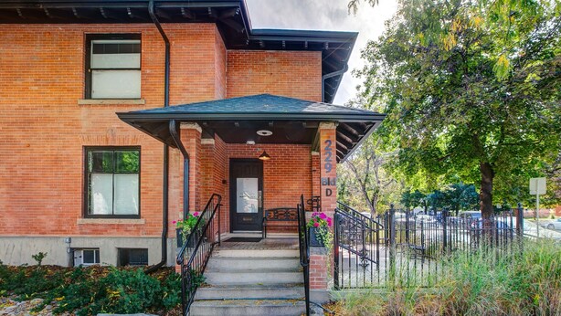 A brick building with a covered entrance, steps, and a metal fence. - The Flats (Fort Collins)
