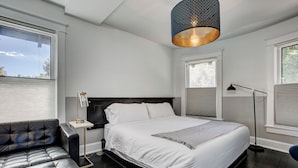 A bedroom with a large bed, a leather sofa, a bedside table, and a floor lamp. - The Flats (Fort Collins)