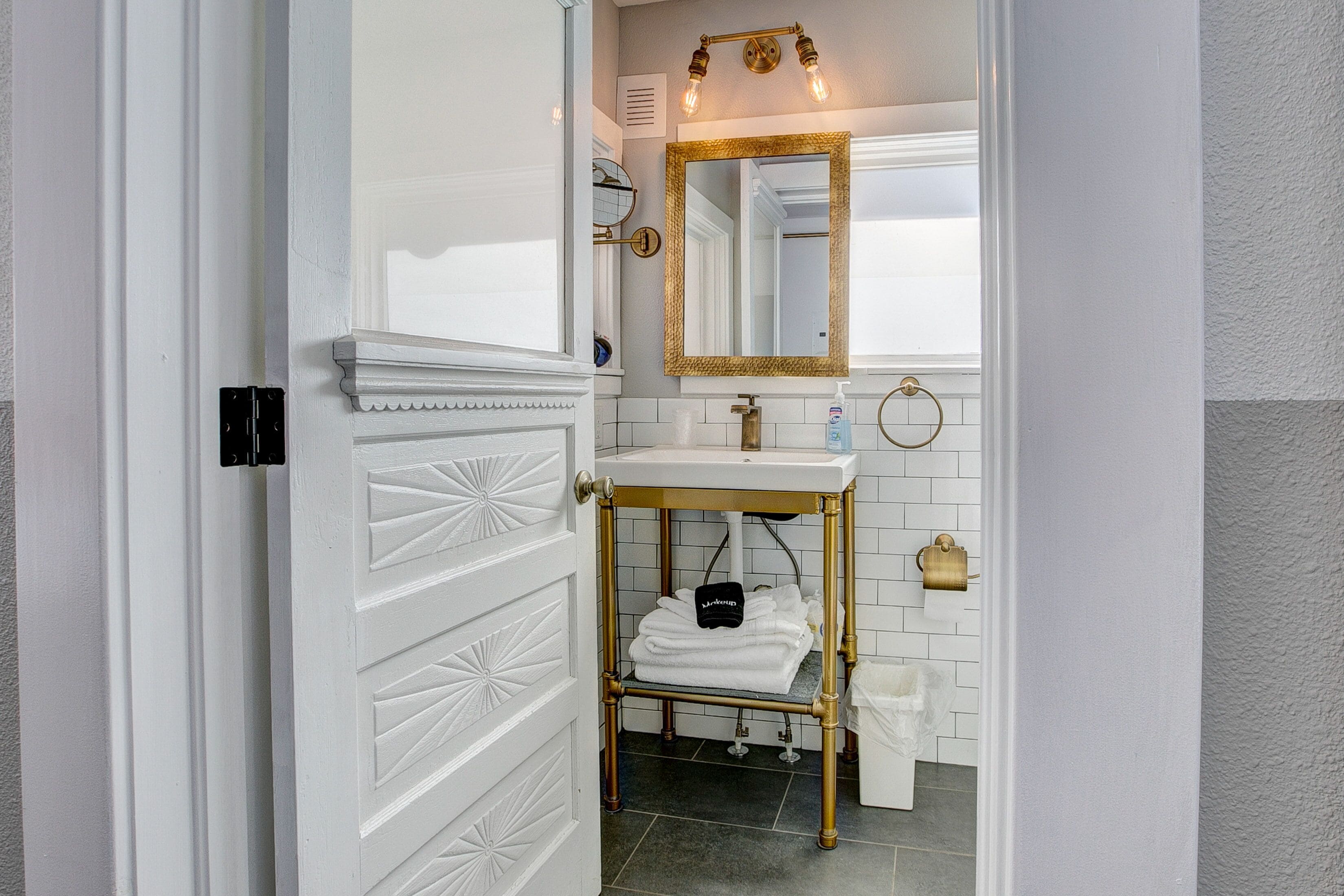 A bathroom with a white door, a gold-framed mirror, a white sink, and a towel rack.