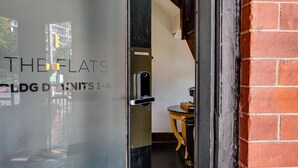 A hotel entrance with a glass door, a sign reading "THE FLATS", and a visible interior including a staircase and a small table. - The Flats (Fort Collins)
