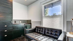 A modern kitchen with dark cabinetry, a built-in refrigerator, and a black leather sofa. - The Flats (Fort Collins)