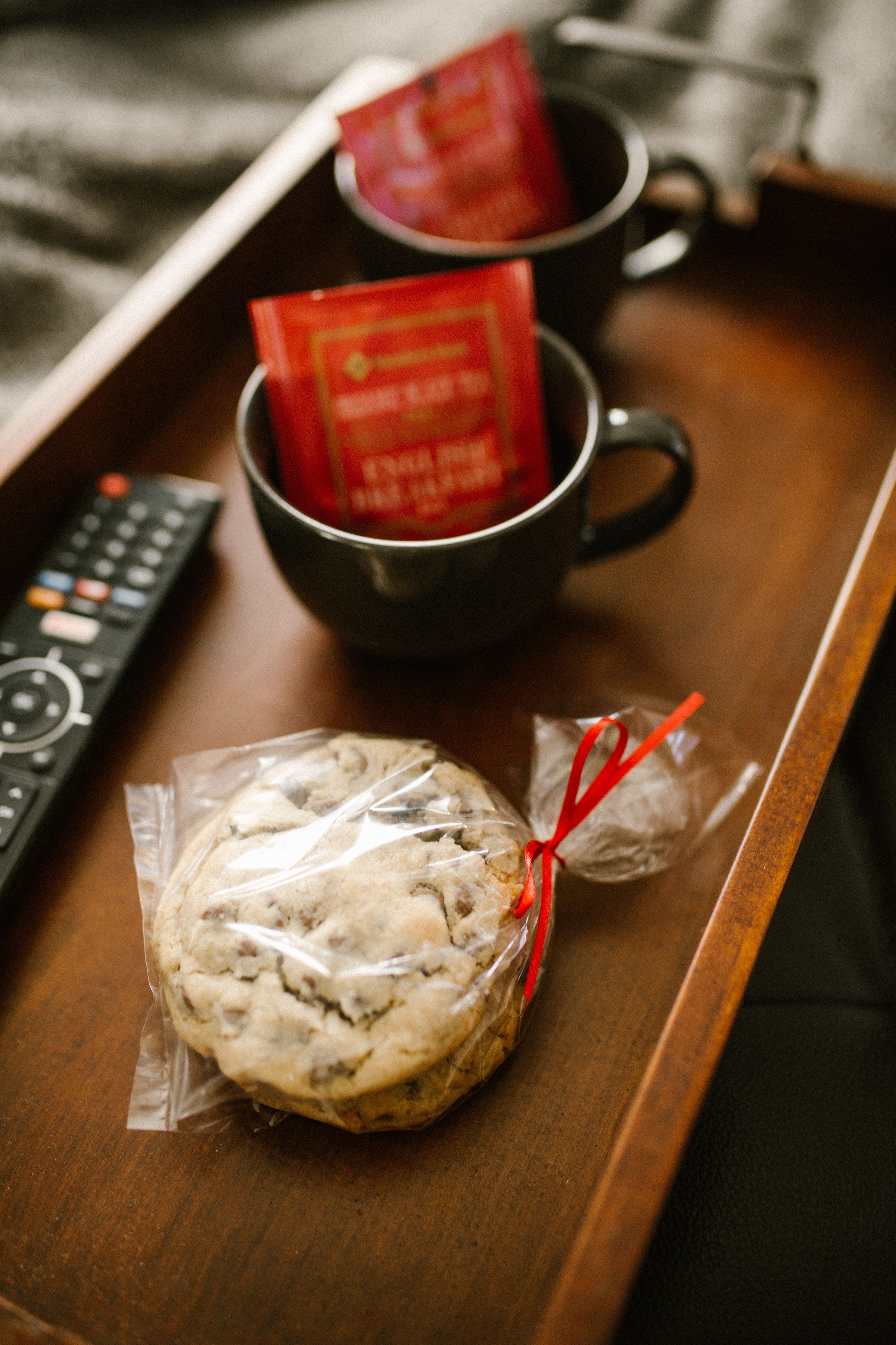A tray with a cookie, two mugs, and a remote control.