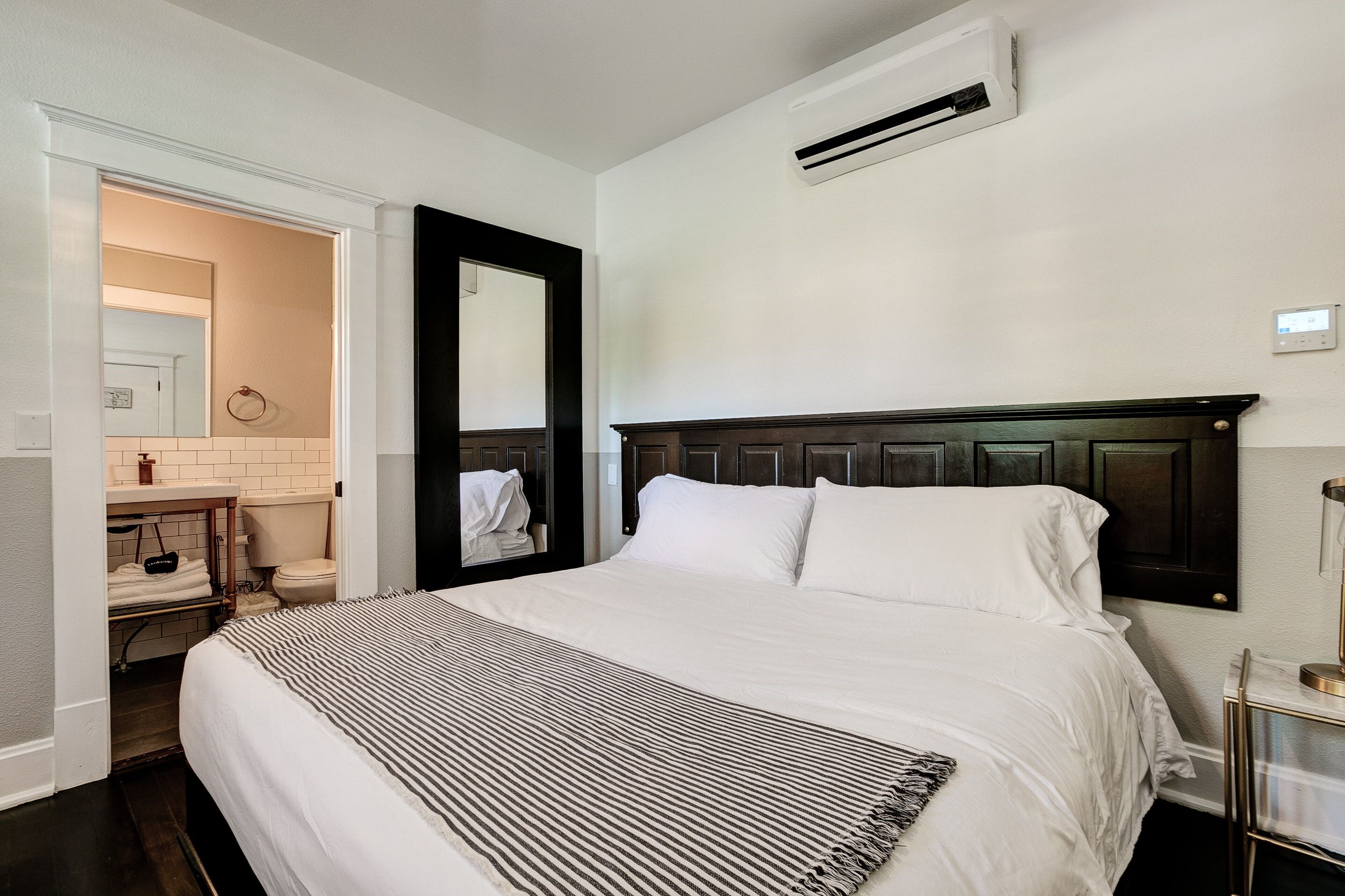 A neatly made bed with a striped blanket, a dark wooden headboard, and a white wall with an air conditioning unit.