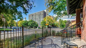 An outdoor seating area with metal chairs and tables, a brick building, and a street with cars and traffic lights in the background. - The Flats (Fort Collins)