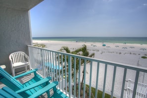 Un balcon avec des chaises turquoise donnant sur une plage parsemée de parasols.