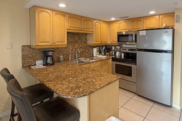 A kitchen with granite countertops, wooden cabinets, a stainless steel refrigerator, an oven, a microwave, and a coffee maker.