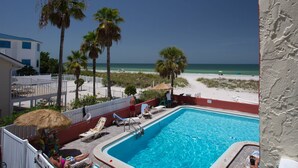 A pool area with lounge chairs, a thatched umbrella, and a view of the beach and ocean.