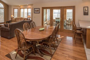 Un coin repas avec une table et des chaises en bois, un canapé et une vue sur l’extérieur grâce à de grandes fenêtres.