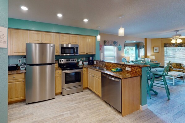 A modern kitchen with stainless steel appliances, wooden cabinets, and a granite countertop. - Beachfront Overlooking the Pool and Beach - Heated Pool, Great Location (Treasure Island)