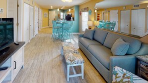 A living room with a sofa, a bench, a television, and a dining area with chairs and a table.