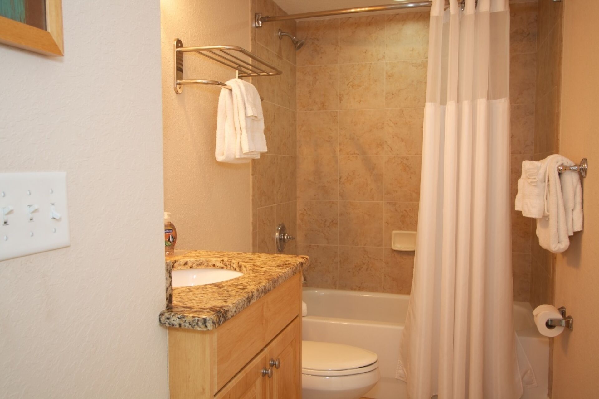 A bathroom with a granite countertop sink, a toilet, a shower with a glass door, and a towel rack.
