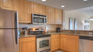 A kitchen with wooden cabinets, stainless steel appliances, granite countertops, and a tiled floor. - Gulf Views from Balcony. Heated Pool. Beautiful Property Directly Across from the Beach! (Treasure Island)