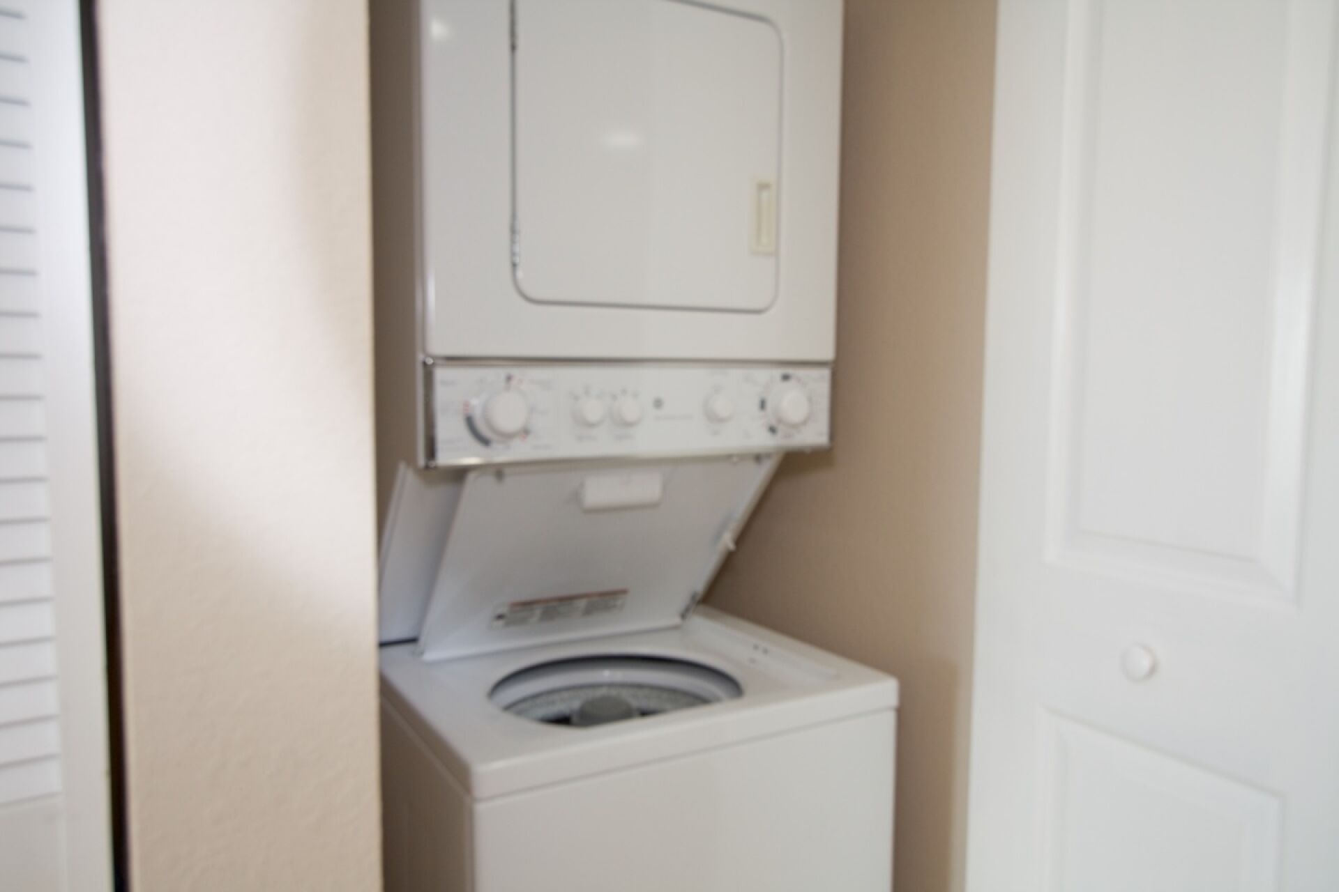 A compact, white laundry room with a front-loading washing machine and a dryer stacked above it.
