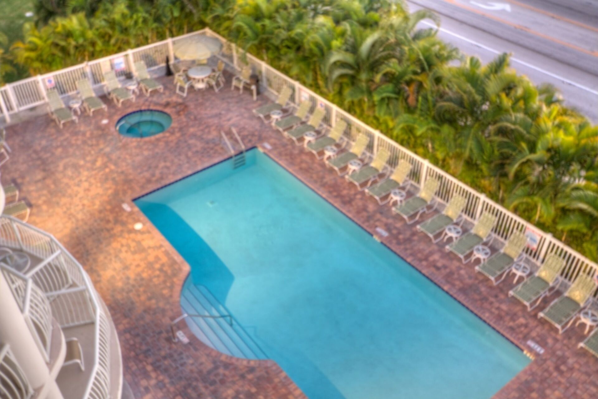 Una piscina rectangular con un jacuzzi circular, rodeada de sillones de descanso y palmeras.