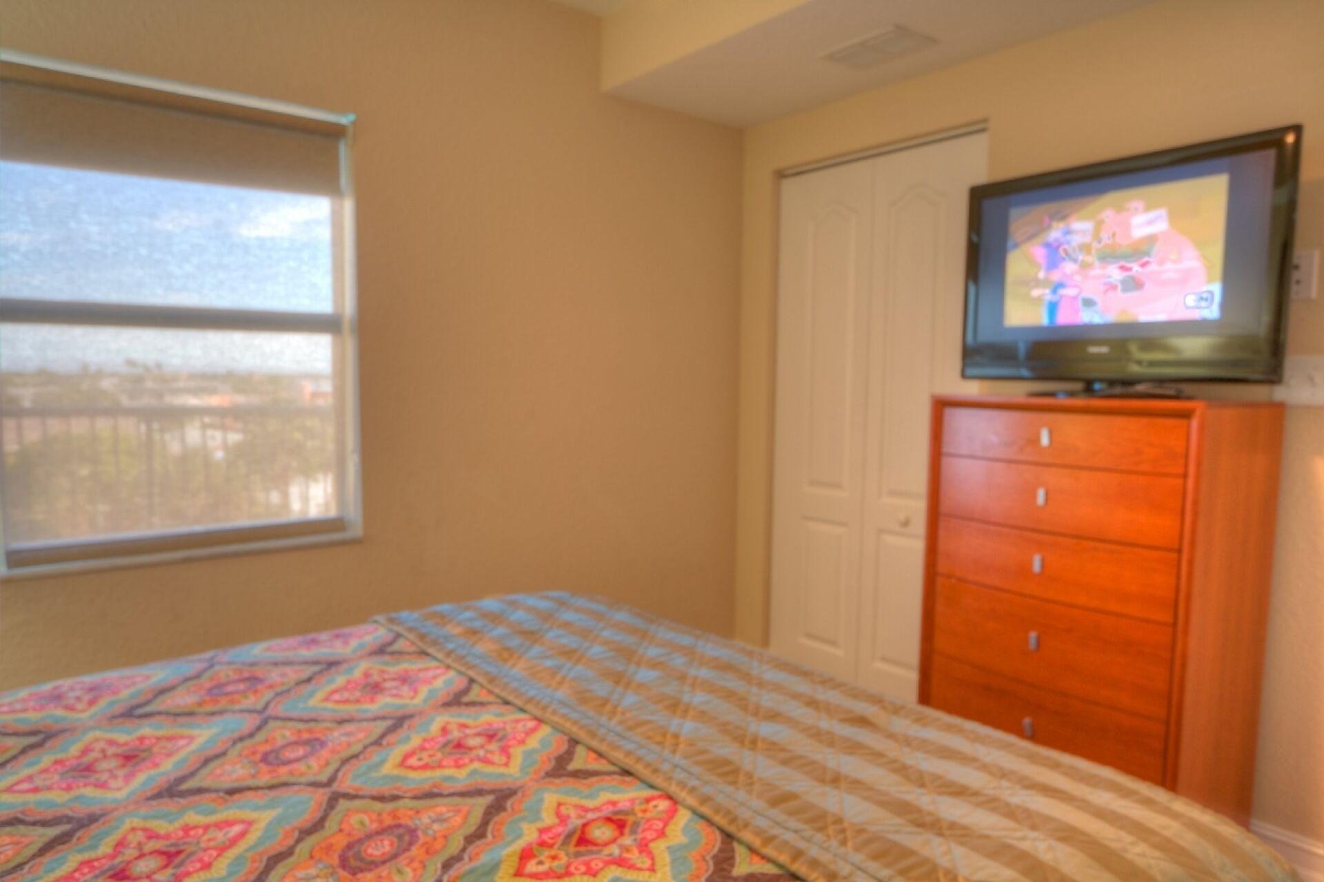 A bedroom with a bed, a dresser, a television, and a window.