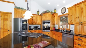 Una cocina moderna con armarios de madera, una isla central, electrodomésticos de acero inoxidable y un reloj en la pared.