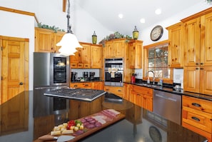 Una cocina moderna con armarios de madera, una isla central, electrodomésticos de acero inoxidable y un reloj en la pared.