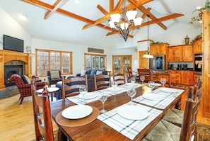 A spacious living room with a fireplace, a dining area set for six, and a kitchen with wooden cabinets.