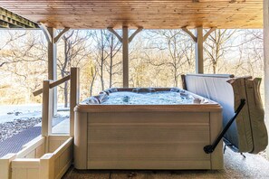 A hot tub under a wooden pergola with a view of leafless trees.