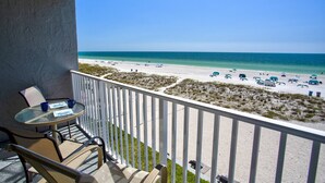 A balcony with a table and chairs, overlooking a beach with umbrellas and lounge chairs.