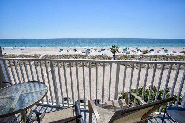 A balcony with a view of a beach, featuring a table and chairs, and a railing. - Escape to Romantic 4th Floor Beachfront Stateroom with Beach View: Beach, Pool, Tiki Bar, Grills (Treasure Island)