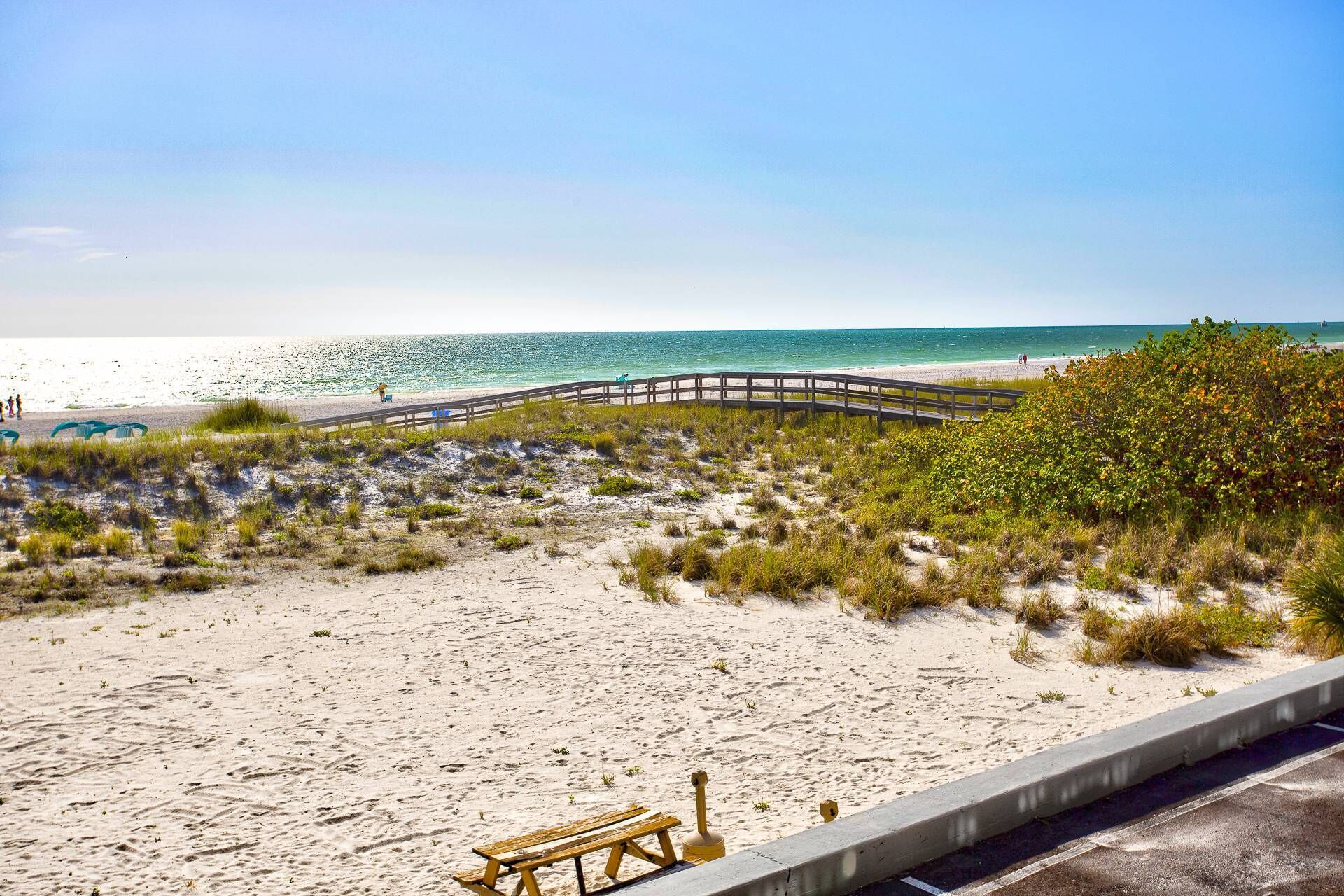 A beach with a wooden walkway, sandy dunes, and a clear view of the ocean.