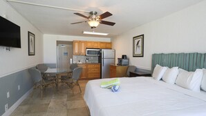 Une chambre d’hôtel comprenant un lit, une table à manger avec des chaises, un coin cuisine et un ventilateur de plafond.