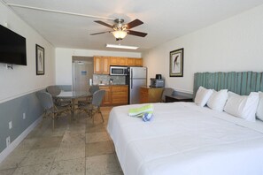 A hotel room with a bed, a dining table with chairs, a kitchenette, and a ceiling fan.