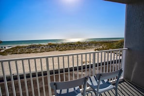 A balcony with white railings overlooking a beach with a wooden walkway and dunes.