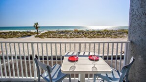 Un balcon avec une table dressée pour deux personnes, donnant sur une plage bordée d’un palmier et offrant une vue dégagée sur l’océan.