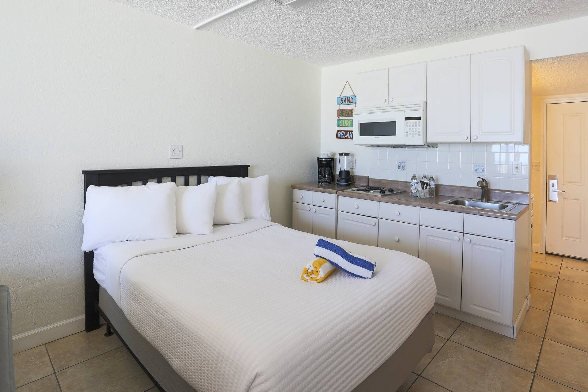 Ein Schlafzimmer mit einem Bett, einer kleinen Küchenzeile mit einer Mikrowelle und einer Tür rechts.