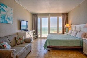 A hotel room with a bed, a TV, a desk, and a balcony with a view of the sea.