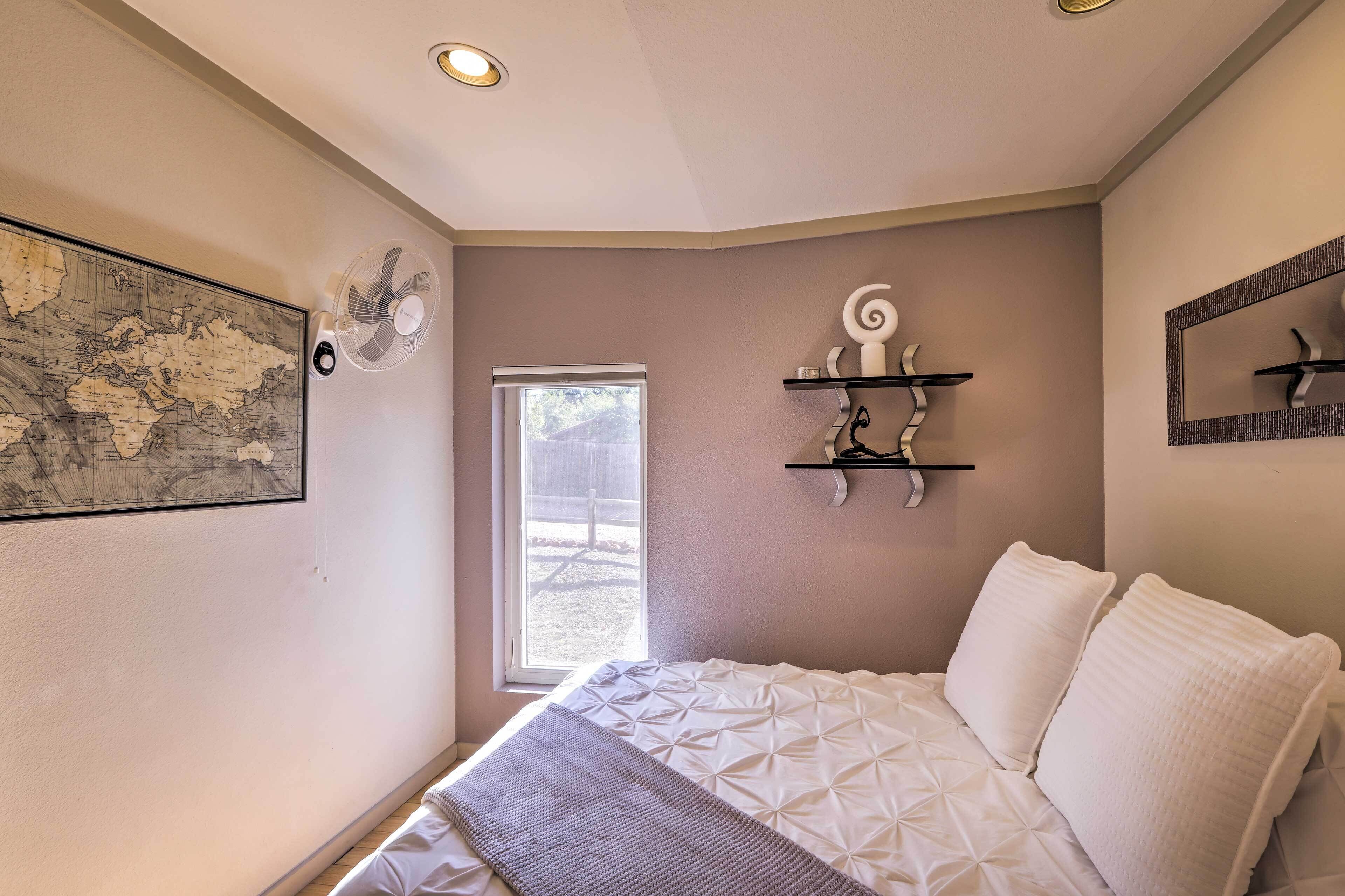 Camera da letto con un letto, una finestra, una ventola a parete, una mappa e una mensola decorativa.