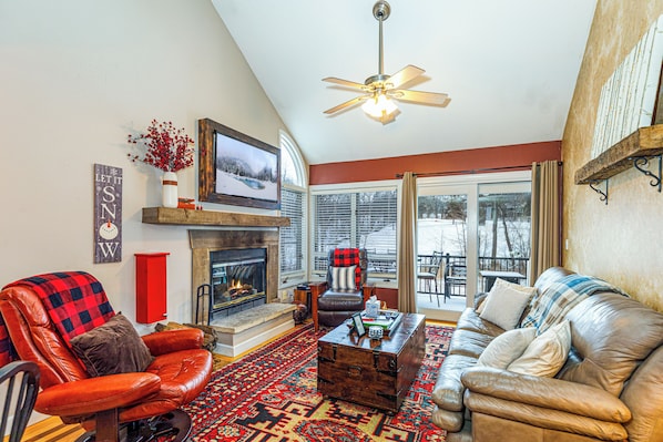 A cozy living room with a fireplace, leather furniture, and a large window overlooking a snowy landscape.