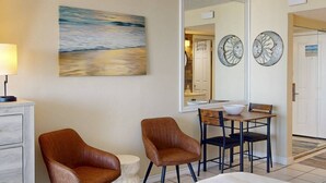 Habitación de hotel con cama, dos sillas, escritorio, lámpara y un cuadro.