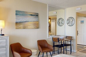 Habitación de hotel con cama, dos sillas, escritorio, lámpara y un cuadro.