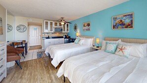 A hotel room with two beds, a dining area, and a kitchenette.