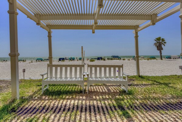 Un quiosco de playa con un banco, una vista despejada de la playa y una palmera al fondo.