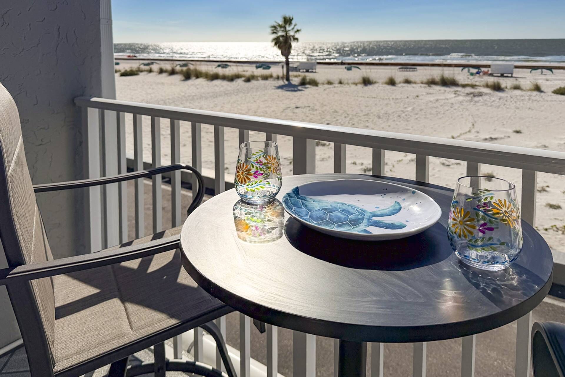 Ein Balkon mit Tisch für zwei Personen, Blick auf einen Strand mit einer Palme und einem klaren Himmel.