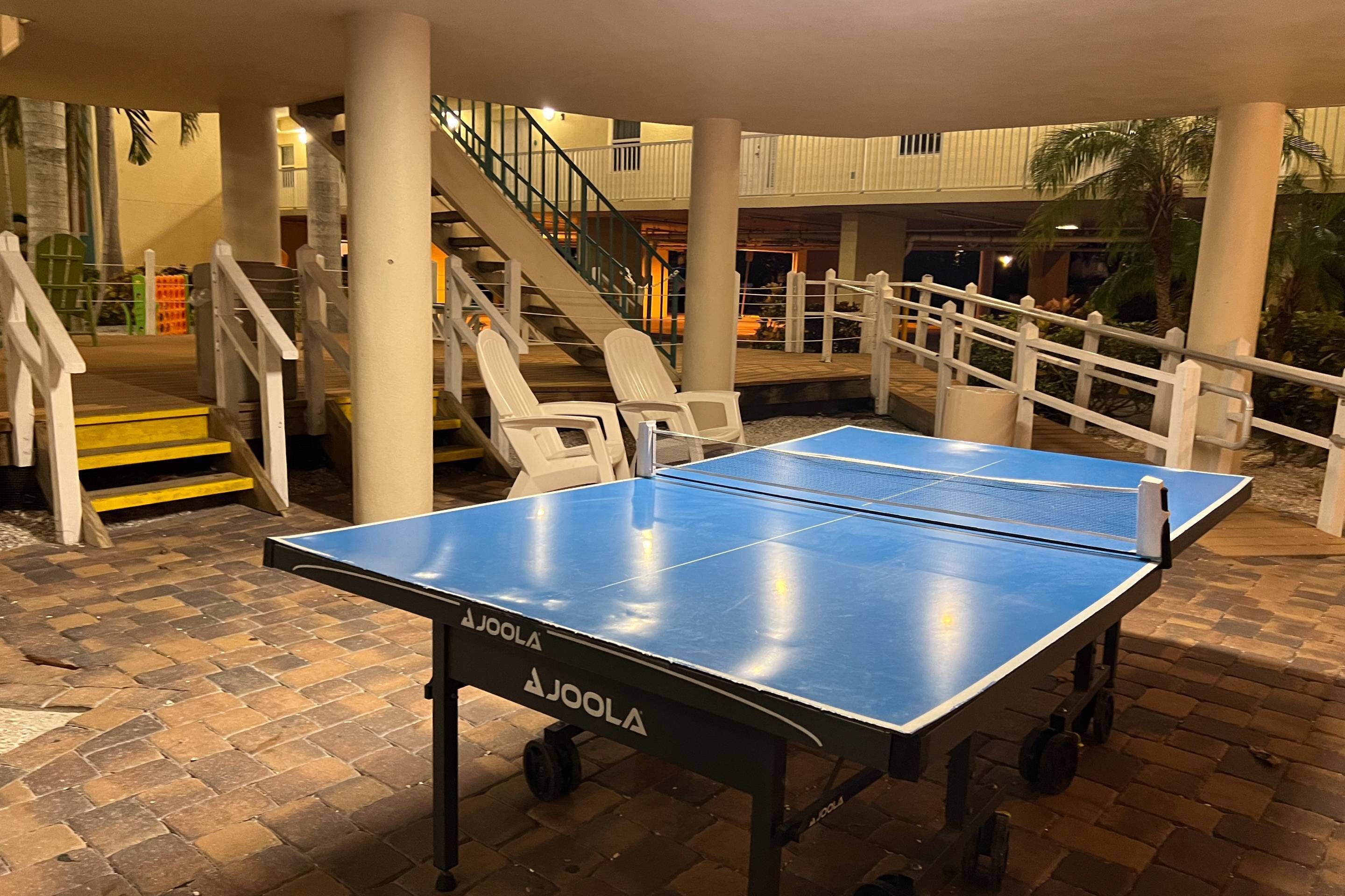 A ping pong table in an outdoor area with a staircase and white railings.