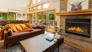 A cozy living room with a fireplace, a leather sofa, and a dining area with a large window overlooking a deck.