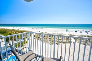 A balcony with a view of a beach with several umbrellas and lounge chairs.