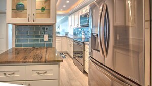 A modern kitchen with a stainless steel refrigerator, white cabinetry, and a glass backsplash. - Beachfront Upgraded Condo. Beach Views! Pool, BBQ, Hot Tub, Volleyball & Shuffleboard, Parking (Treasure Island)